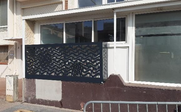 Panneau ajouré anthracite à motif chevrons, monté sur un muret devant la devanture d'un commerce à Canet-en-Roussillon