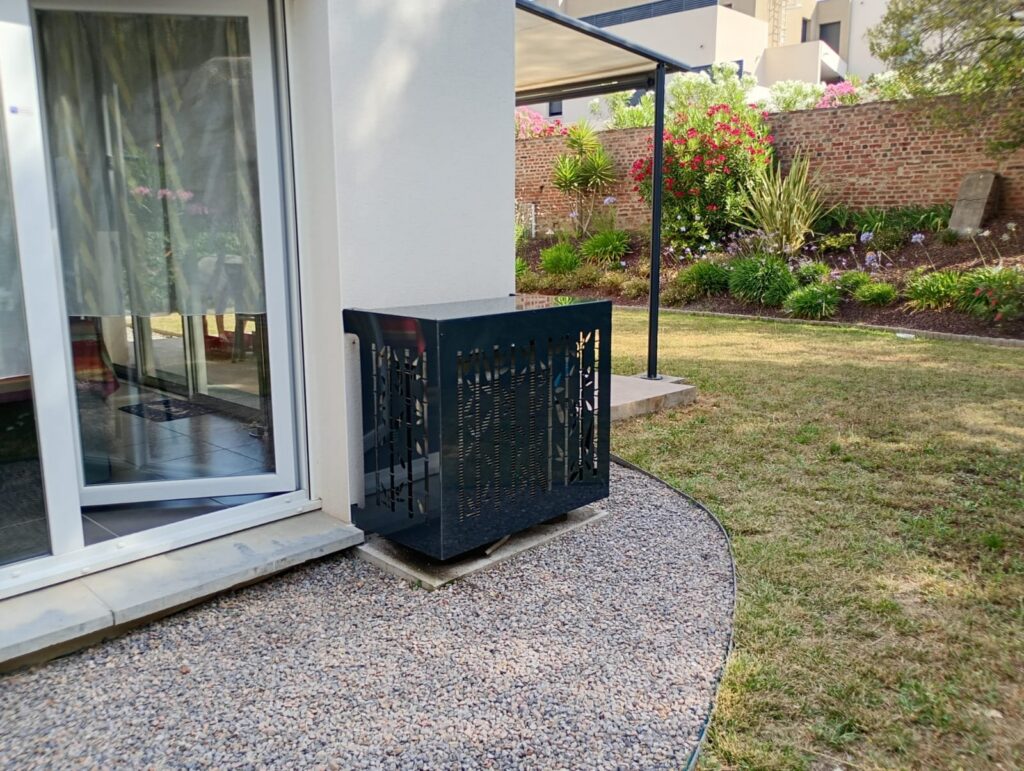 Cache-climatisation anthracite à motif bambou, posé à l'angle d'une baie vitrée à Thuir