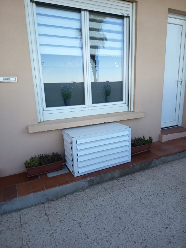 Cache-climatisation sur-mesure blanc à persiennes sous une fenêtre, maison face à la mer à Canet-en-Roussillon